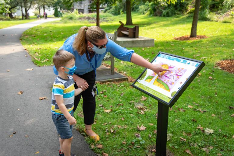 Mother and boy stand alongside storywalk display in a sunny park