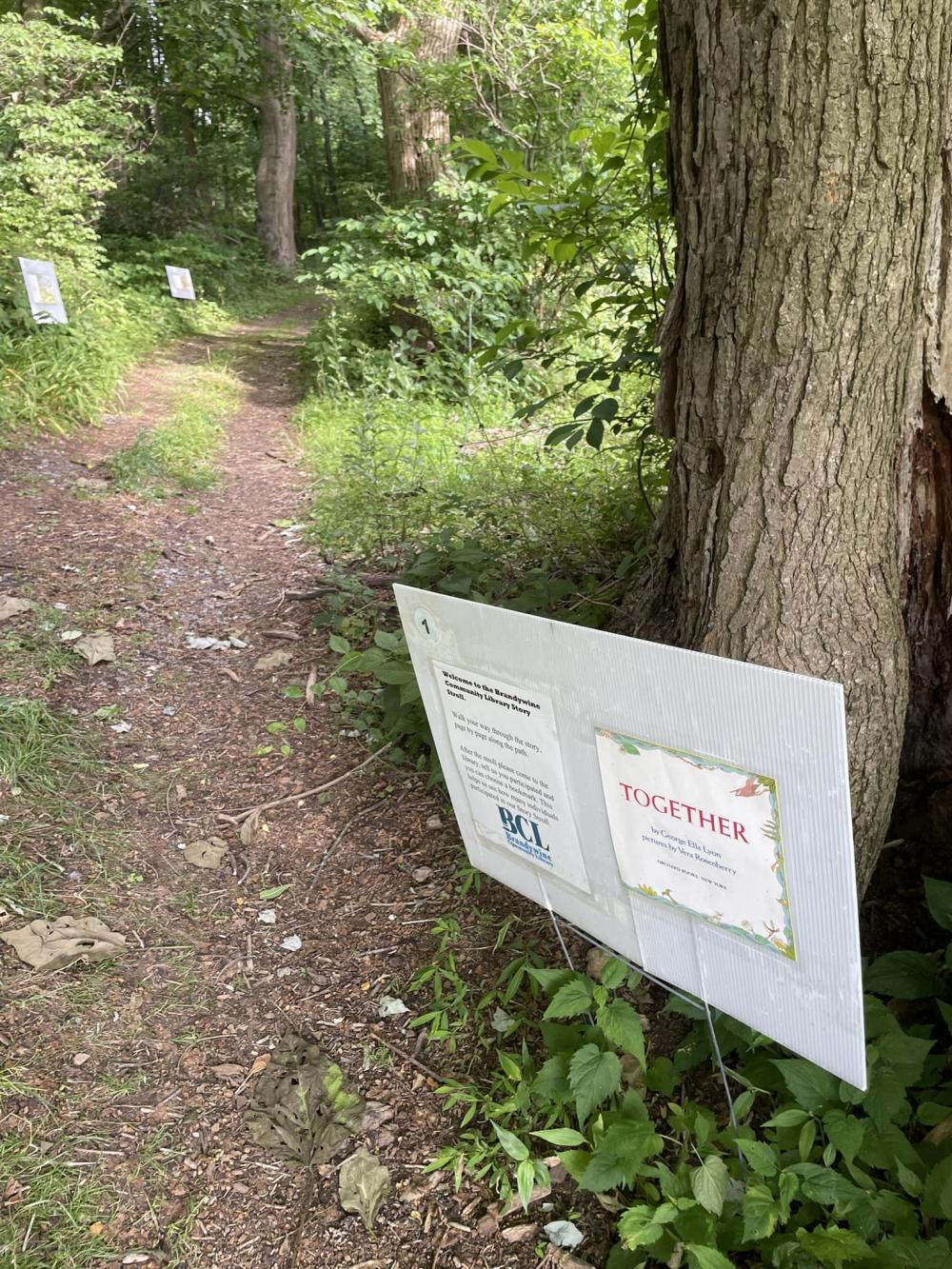 yard signs with story pages line a shaded, wooded trail