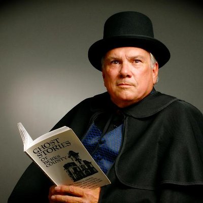 Charles Adams in a top hat and holding one of his ghost story books