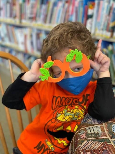 Anakin, a young boy, wearing a mask and orange cut-out sunglasses, playfully holding his hands to his head as if he had animal ears.