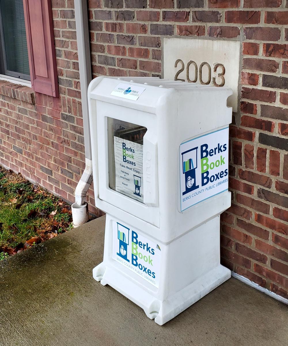 White, plastic newspaper box sitting outside a brick building with books inside