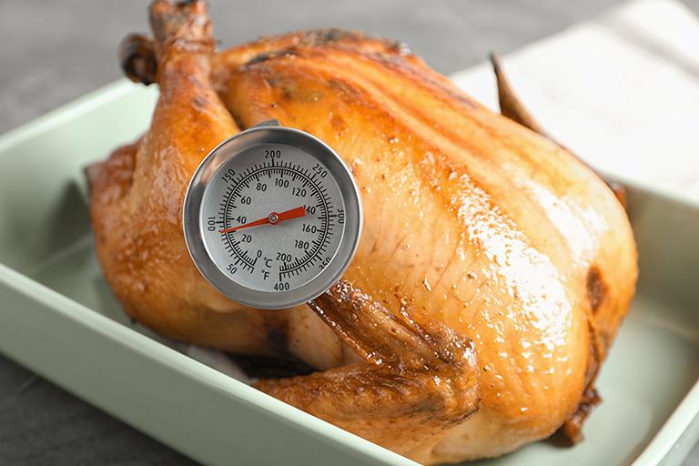 golden turkey in oven pan with food thermometer stuck inside