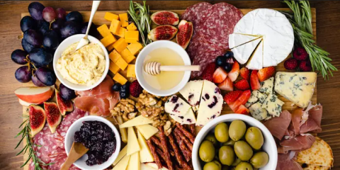 meats, cheeses, fruits, crackers on a wooden food board
