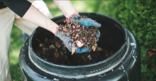 A person holding dirt over a composting bucket